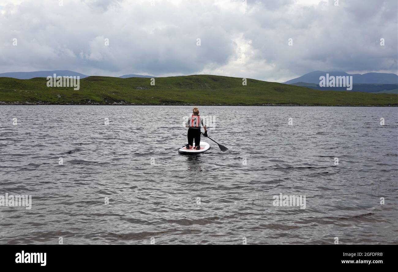 Señora mayor arrodillándose en Stand up Paddle Board, Loch Laidon, Perthshire Scottish Highlands, Reino Unido Foto de stock