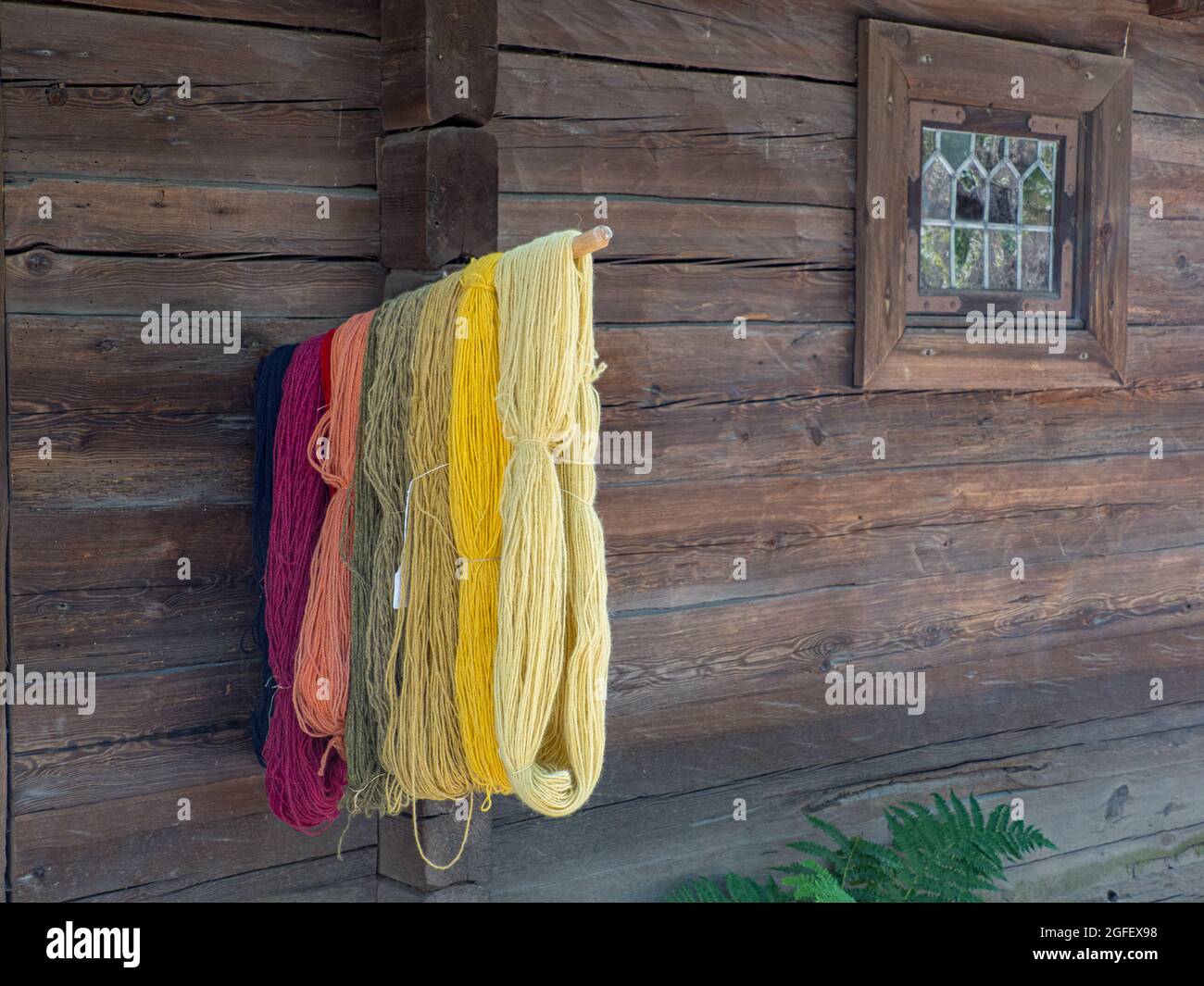 Hilados teñidos caseros colgados fuera de una antigua casa de madera. Foto de stock
