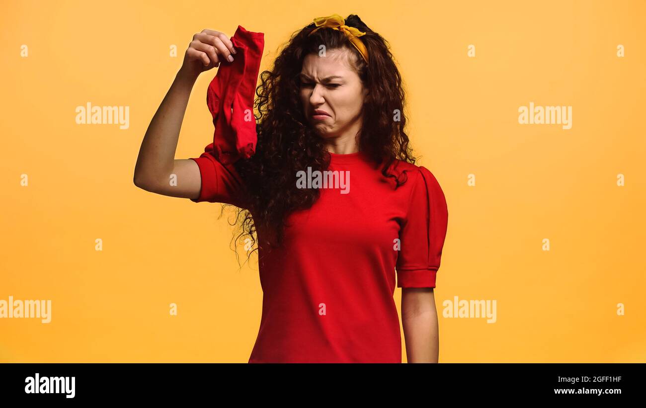 una mujer disgustada sosteniendo unos calcetines olorosos aislados sobre naranja Foto de stock