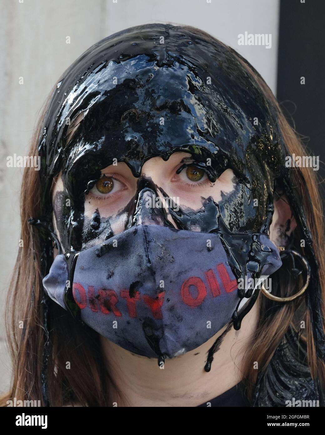 Londres, Reino Unido. Una mujer vierte aceite falso sobre su cabeza en una protesta para destacar las preocupaciones ambientales vinculadas a la industria de la moda rápida. Foto de stock
