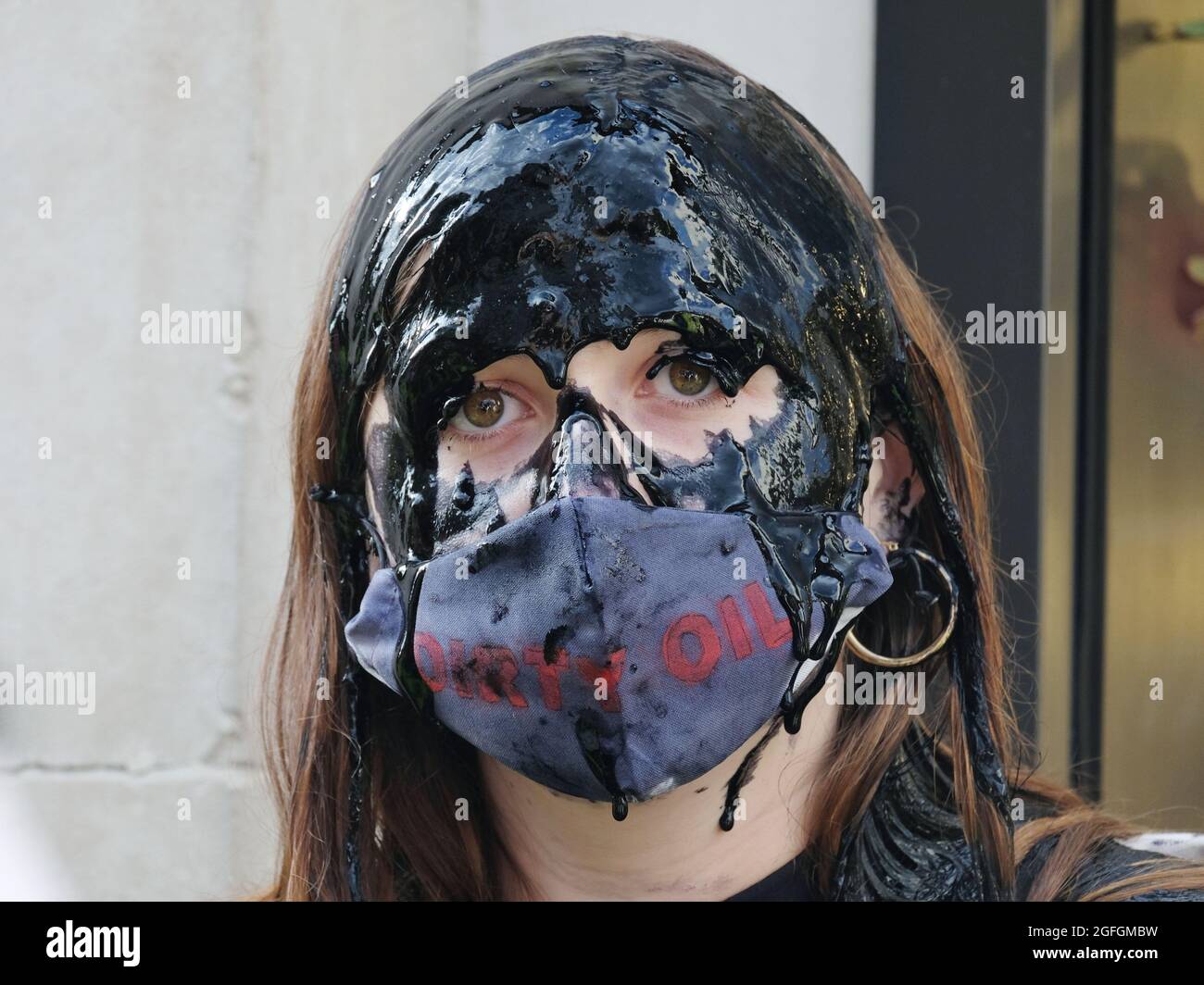 Londres, Reino Unido. Una mujer vierte aceite falso sobre su cabeza en una protesta para destacar las preocupaciones ambientales vinculadas a la industria de la moda rápida. Foto de stock