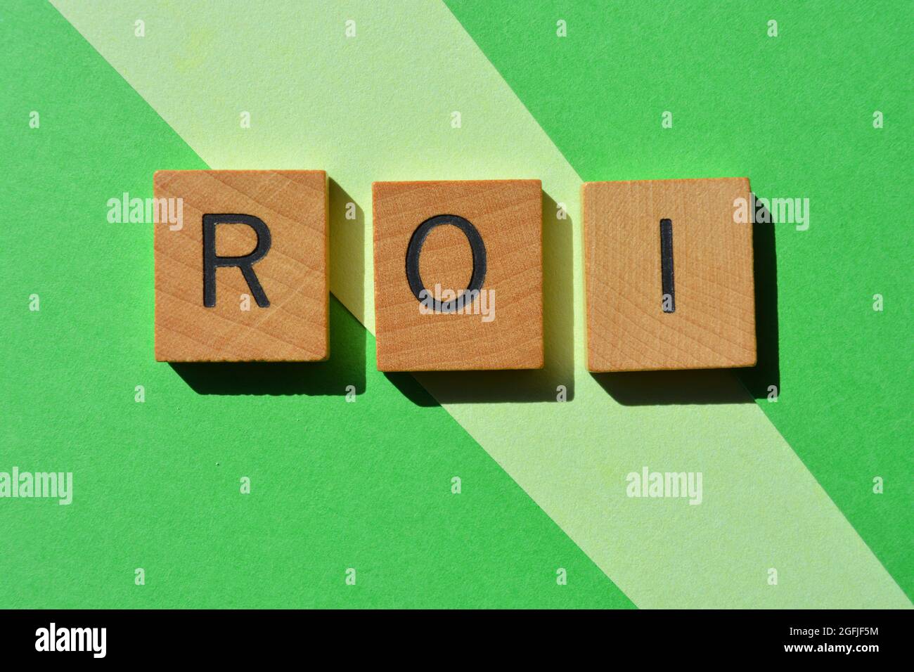 ROI, acrónimo de Return on Investment, en letras del alfabeto de madera aisladas sobre fondo verde Foto de stock