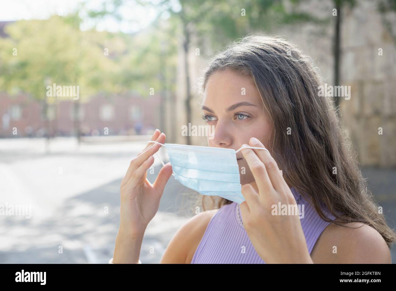 Mujer joven que se ajusta una máscara protectora al aire libre debido a Covid Foto de stock