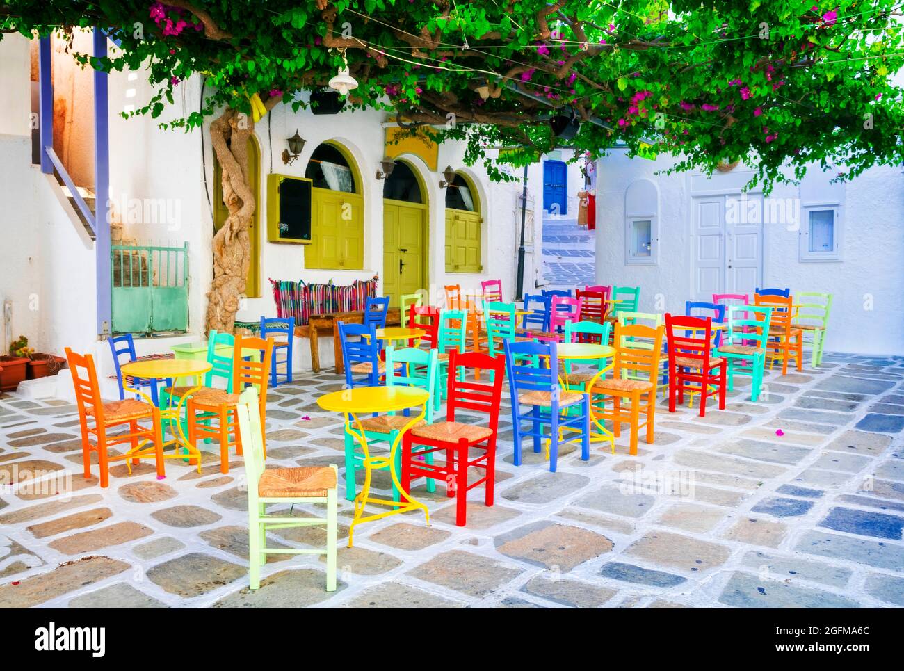 Tabernas griegas tradicionales en las calles. Isla iOS, casco antiguo de Chora. Restaurante con coloridas sillas típicas. Cyclades, Grecia Foto de stock