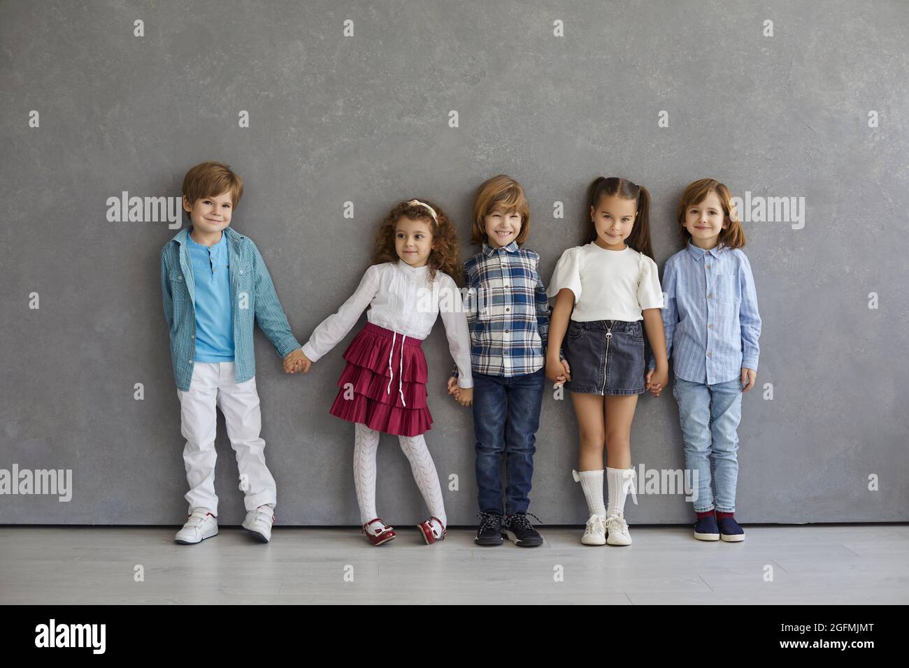 Retrato de niños y niñas pequeños, lindos y felices, con ropa informal de pie contra la pared gris. Foto de stock