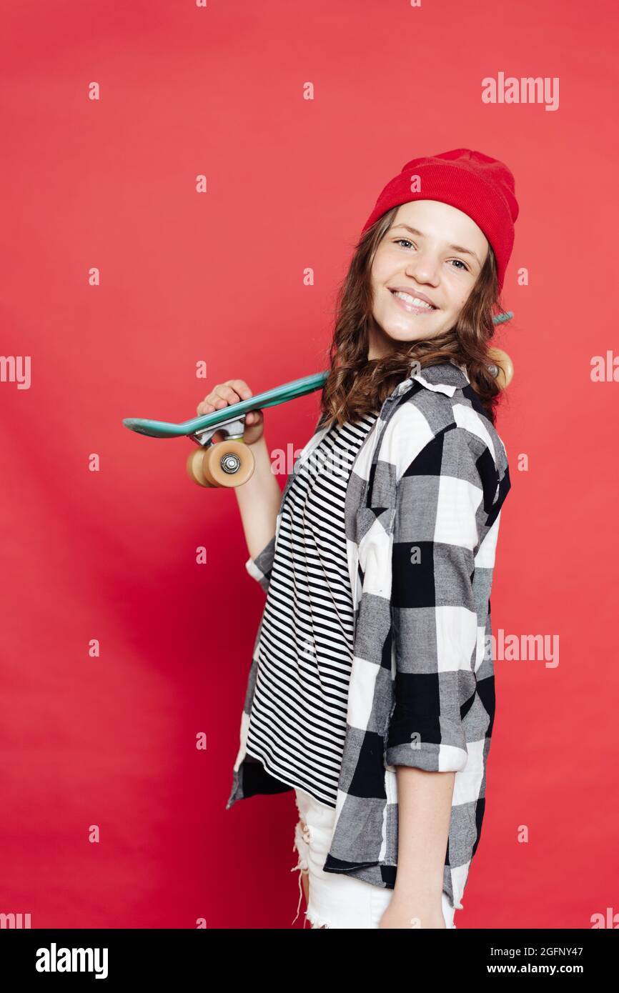 Feliz niña adolescente con estilo con gorro rojo, pantalón corto blanco y  camisa a cuadros posando con penny board sobre fondo rojo Fotografía de  stock - Alamy
