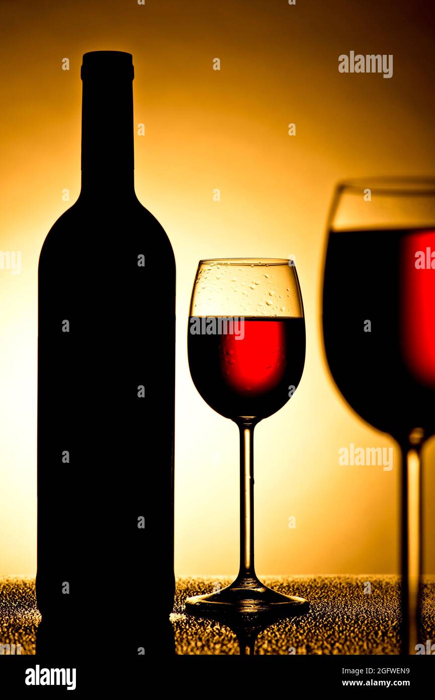 vasos con vino tinto y botella con retroiluminación Foto de stock