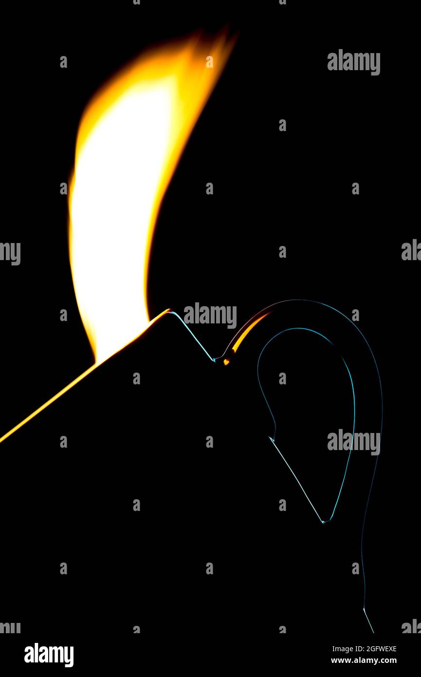 taza con retroiluminación y llama de un encendedor Foto de stock