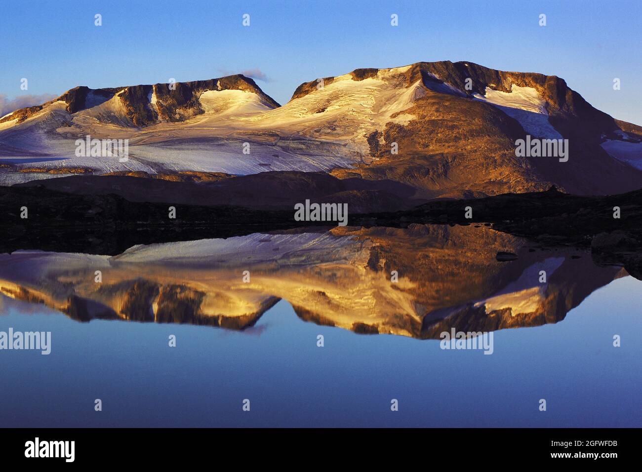 Luz a primera hora de la mañana en los picos Fannaraken con un reflejo similar a un espejo en un lago glacial, Noruega, Parque Nacional Jotunheimen, Fannaraken Foto de stock