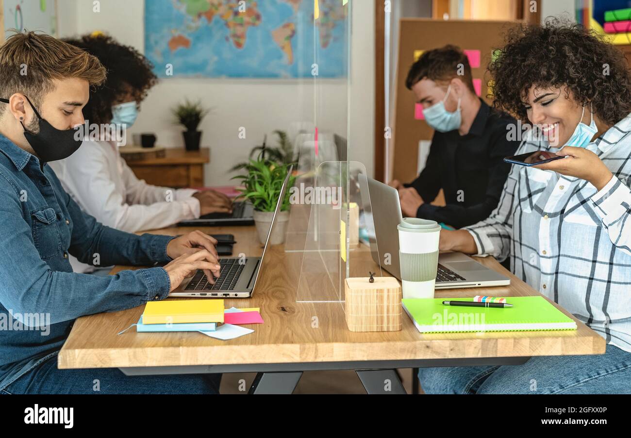 Jóvenes multirraciales que usan la computadora en el espacio creativo de trabajo conjunto mientras usan máscara facial - Concepto de tecnología de salud y negocios Foto de stock