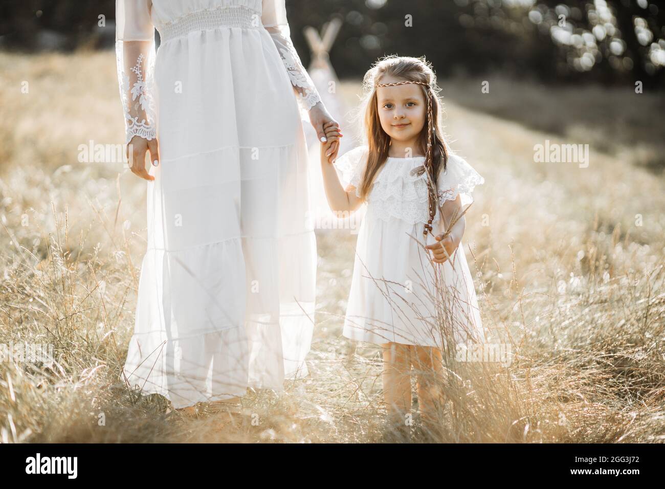 Primer plano de niña feliz con vestido blanco, sostiene la mano de su madre  y camina juntos en el campo de verano. Madre e hija en boho vestido pasar  tiempo al aire