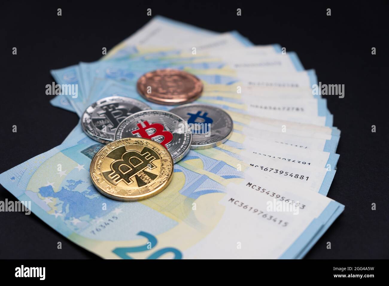 Bitcoins de varios colores encima de billetes de banco de 20 euros. Bitcoins sobre veinte billetes de euros sobre fondo oscuro. Concepto de criptomoneda, bitcoin y. Foto de stock