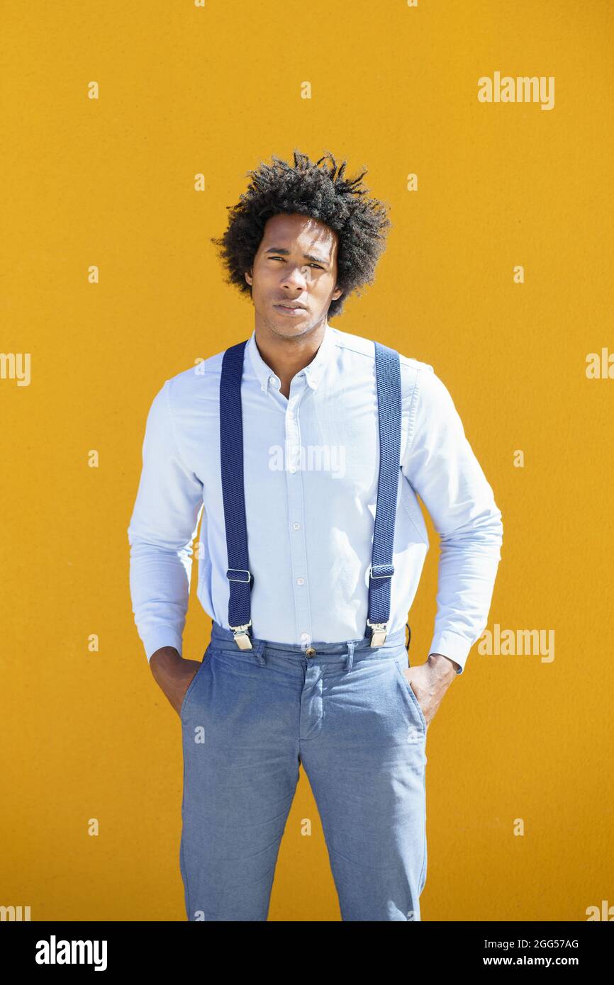 Hombre negro con pelo afro sobre fondo urbano amarillo con camisa y tirantes. Foto de stock