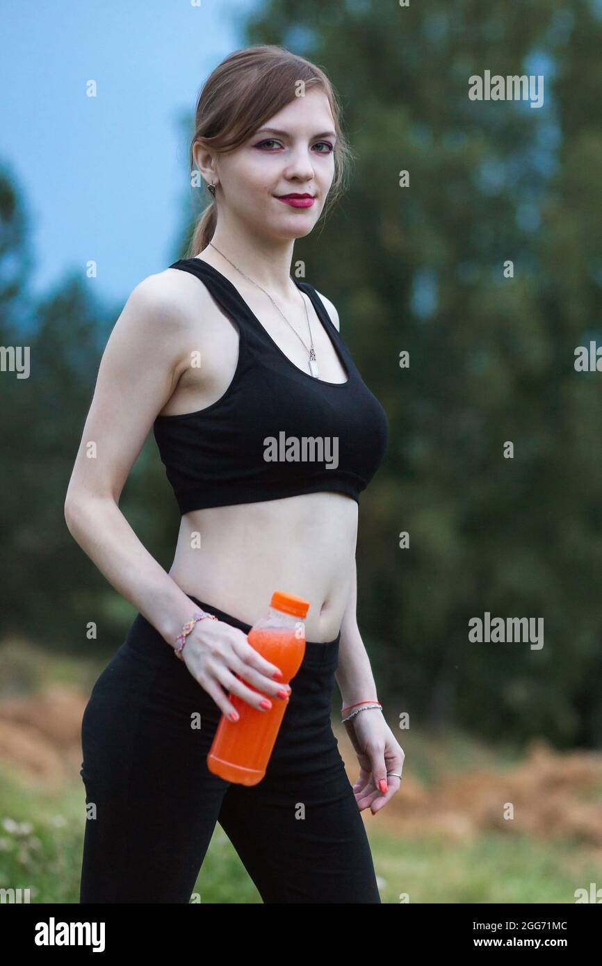 Mujer con ropa deportiva hidratándose bebiendo jugo de naranja vibrante  durante el entrenamiento. Por la noche o por la mañana en la naturaleza  Fotografía de stock - Alamy