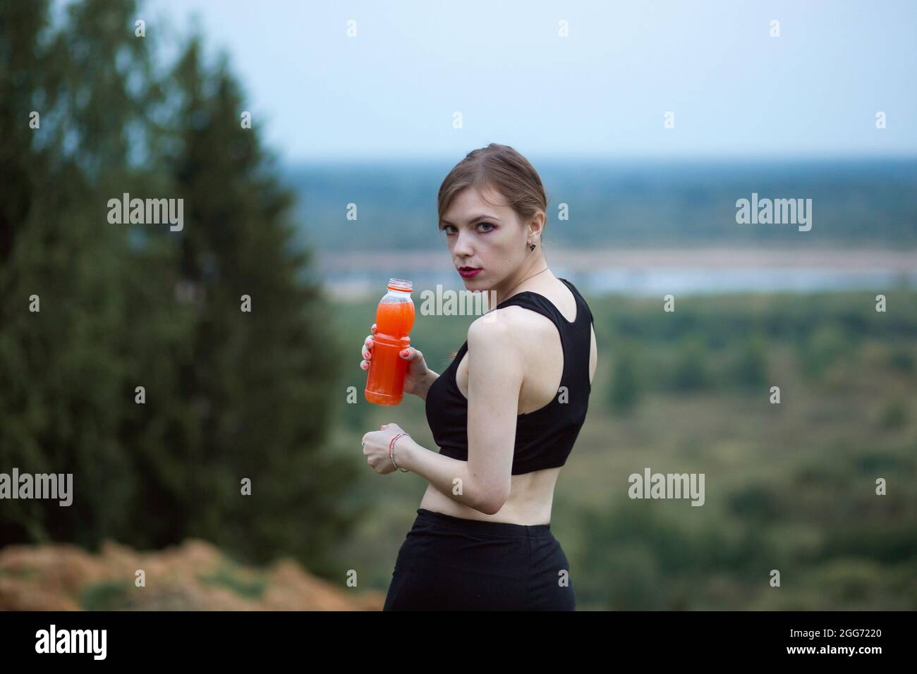 Mujer con ropa deportiva hidratándose bebiendo jugo de naranja vibrante  durante el entrenamiento. Por la noche o por la mañana en la naturaleza  Fotografía de stock - Alamy