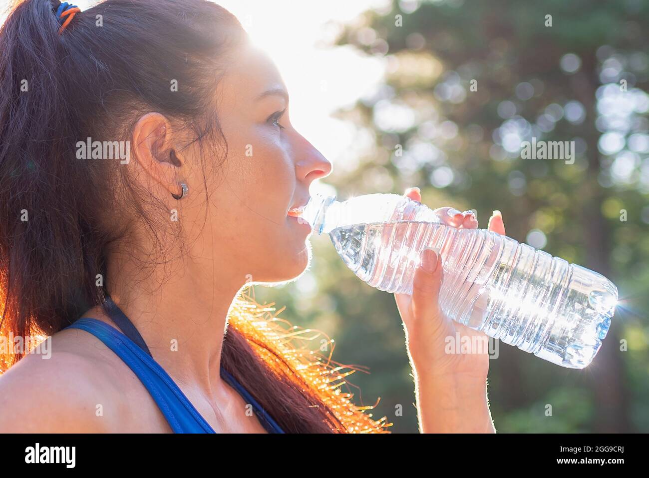 Niña bebiendo agua de botella en un bosque. Mujer joven sosteniendo una  botella de agua en el forest.Positive dama en ropa deportiva tienen  descanso después de correr, j Fotografía de stock -