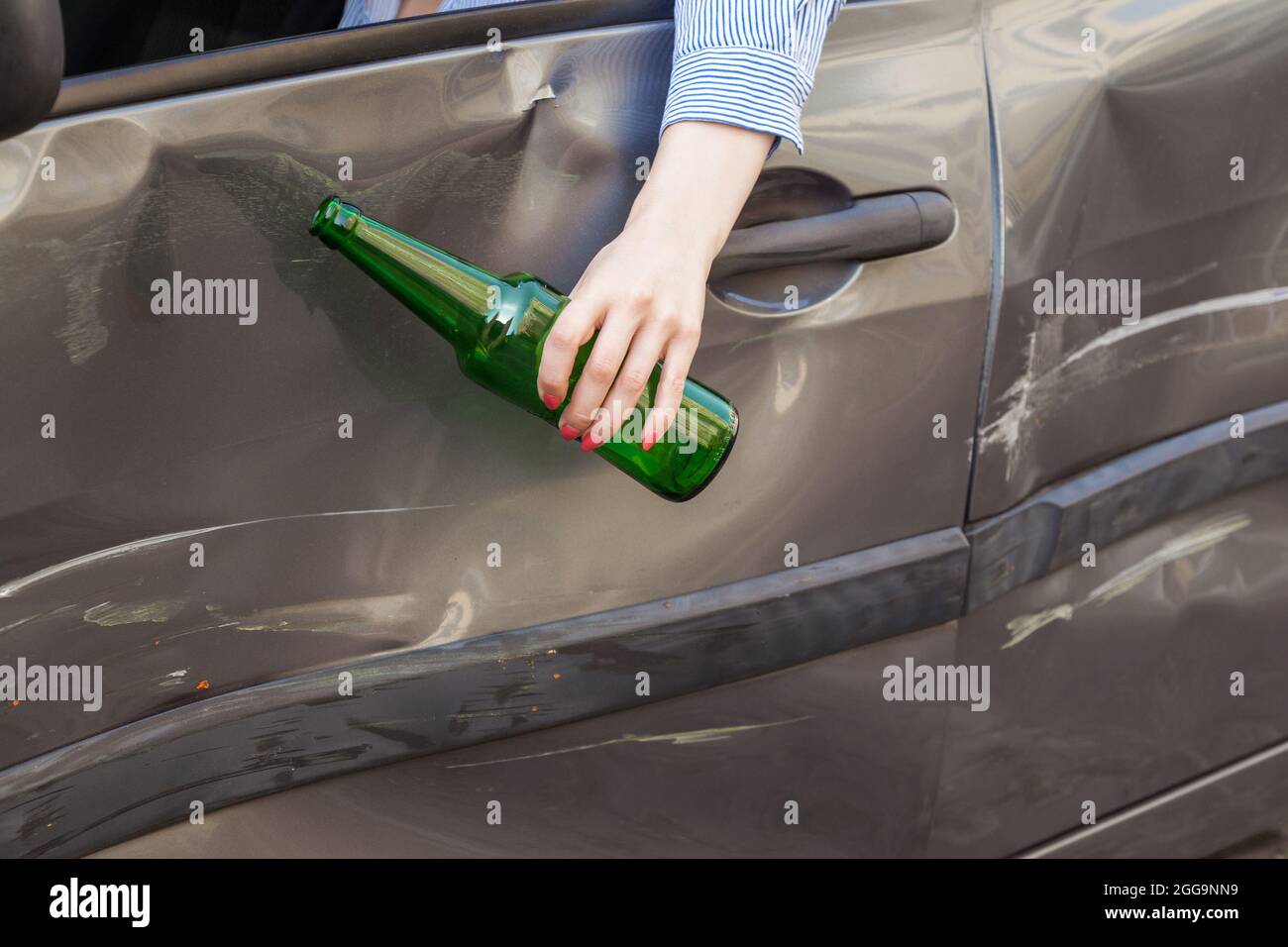 Retrato sin rostro de la mano femenina colgando de la ventana del coche con una botella de bebida alcohólica, avería debido a conductor borracho, delitos de tráfico borracho dr Foto de stock