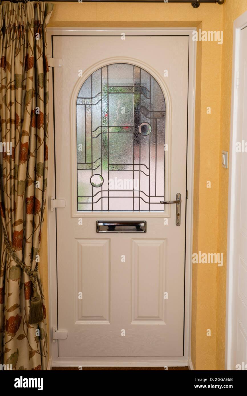 Un vestíbulo en una casa del Reino Unido con una puerta frontal blanca con una ventana de cristal esmerilado que da al jardín frontal y a una cortina Foto de stock
