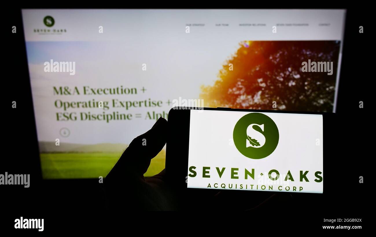 Persona que sostiene el smartphone con el logotipo de la compañía estadounidense Seven Oaks Acquisition Corp. En la pantalla frente al sitio web. Enfoque en la pantalla del teléfono. Foto de stock