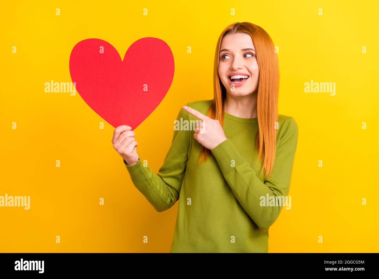 Foto de divertido jengibre cabello joven dama punto mirada corazón desgaste  verde suéter aislado sobre fondo de color amarillo Fotografía de stock -  Alamy