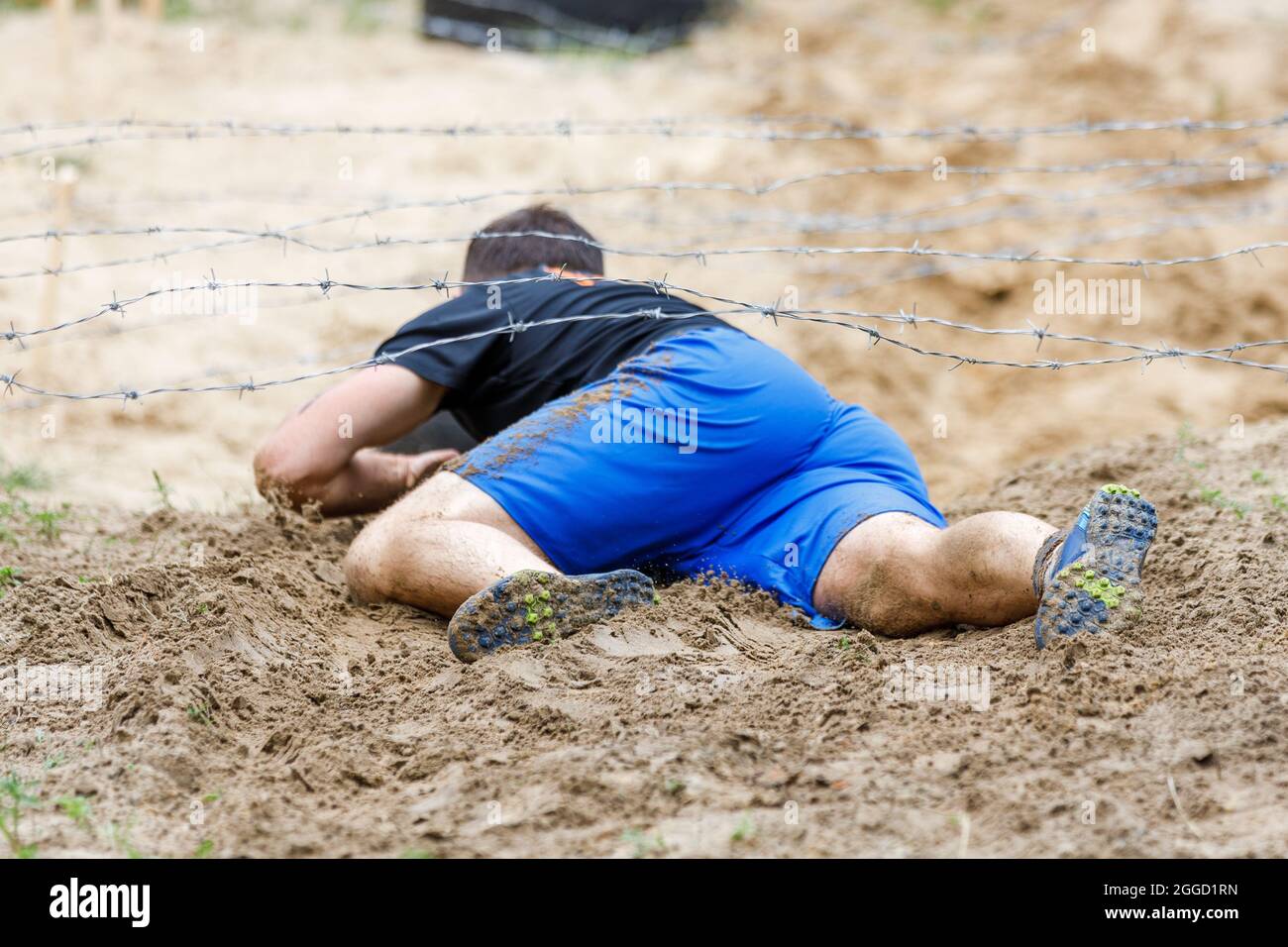 Sportsman trepando bajo un obstáculo de alambre de púas en su curso en carrera de obstáculos Foto de stock
