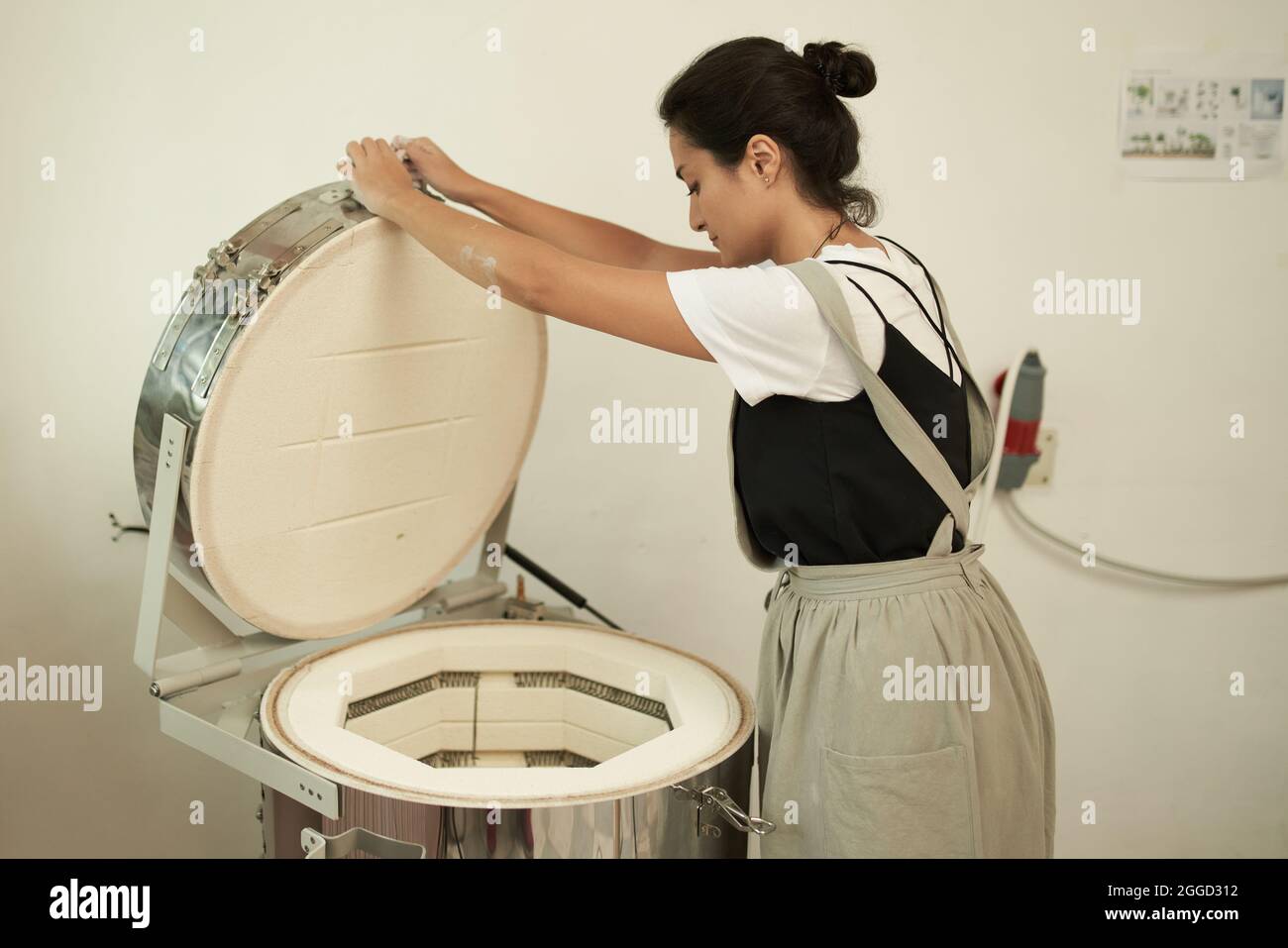 Vista lateral de la joven artesana abriendo horno eléctrico para hornear  arcilla mientras trabaja en taller de cerámica Fotografía de stock - Alamy