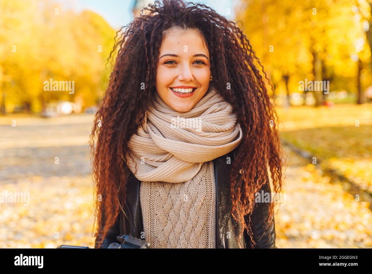 Atractiva mujer de pelo afro con una sonrisa blanca como la nieve con una cálida bufanda Camine en el parque de otoño en un soleado día cálido. Retrato de mujer feliz al aire libre Foto de stock