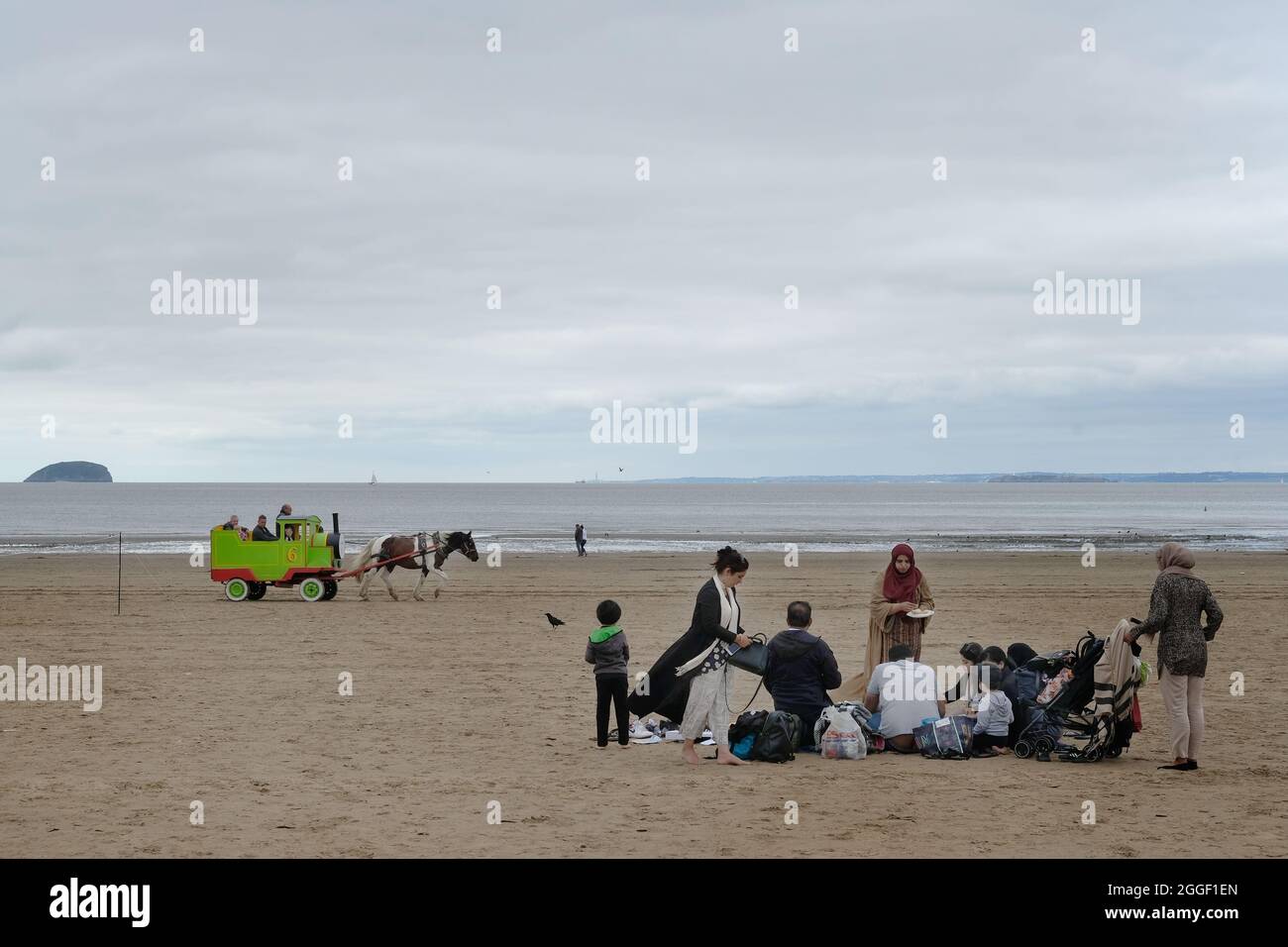 Una familia asiática sentada en una playa gris y nublada de Weston Super Mare, Reino Unido Foto de stock