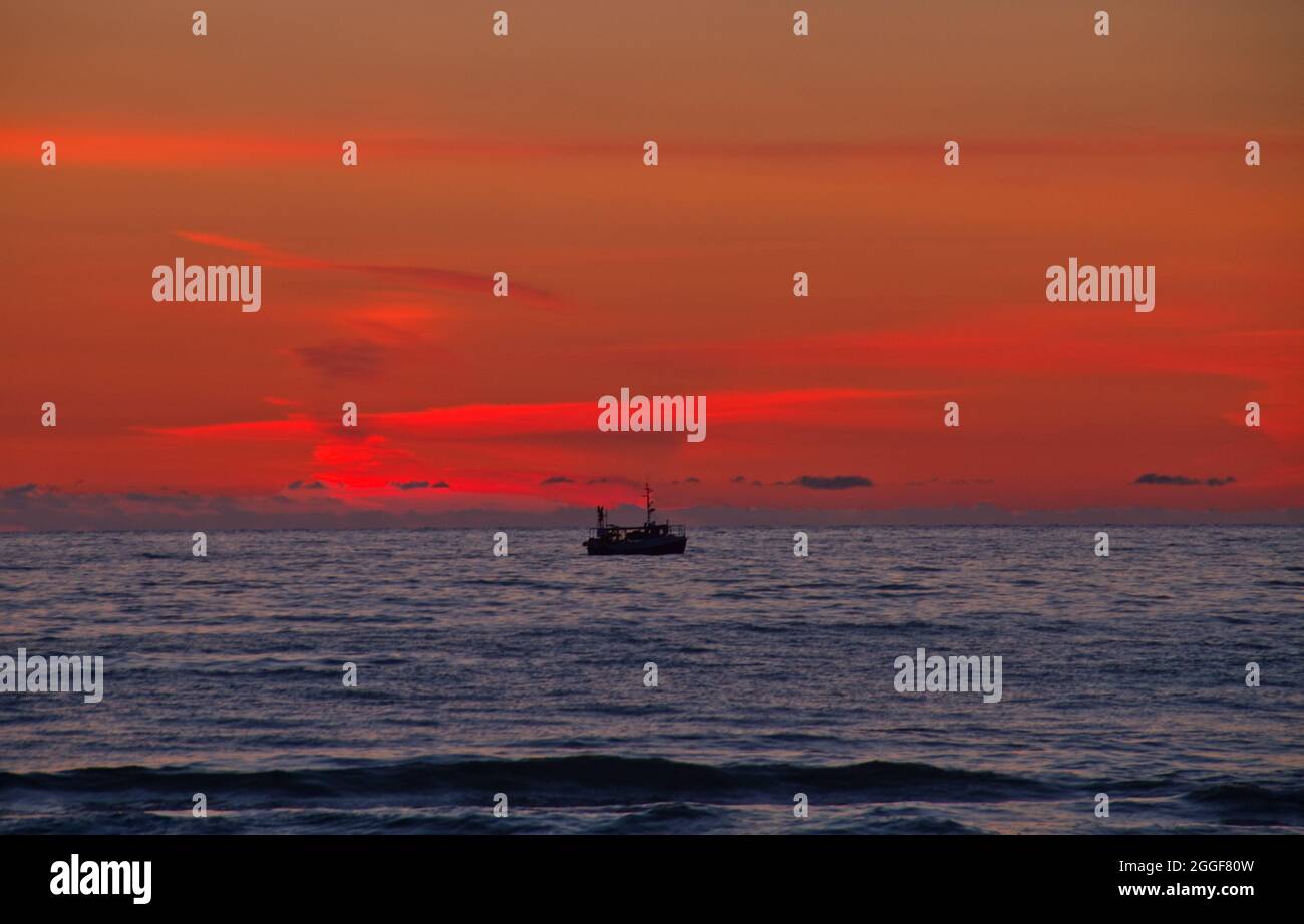 Silueta del barco pesquero en un mar tranquilo justo después de la puesta de sol Foto de stock