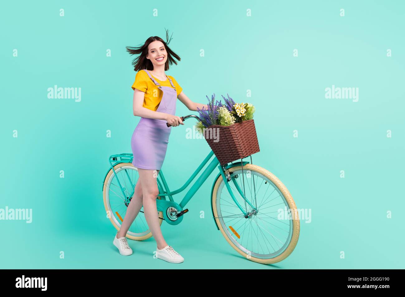 Foto de cuerpo completo de alegre joven dama feliz viento soplar cabello montar bicicleta asilado sobre fondo de color pastel de téal Foto de stock