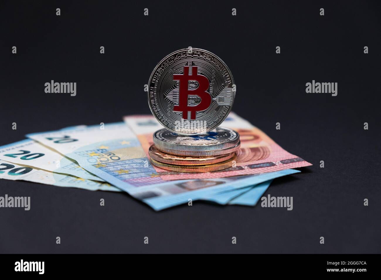 Bitcoins con el símbolo rojo encima de los billetes de banco de 20 y 10 euros. Bitcoins en billetes de diez y veinte euros sobre fondo oscuro. Foto de stock