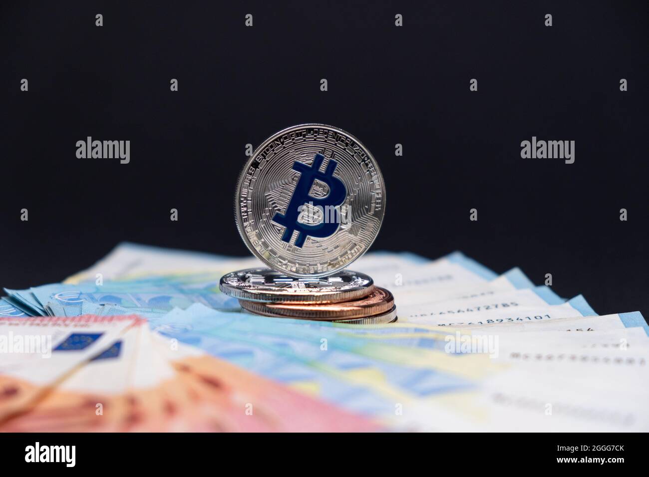 Los bitcoins con el símbolo azul en foco se encuentran encima de los billetes de banco de 20 y 10 euros. Bitcoins en billetes de diez y veinte euros sobre fondo oscuro. Foto de stock