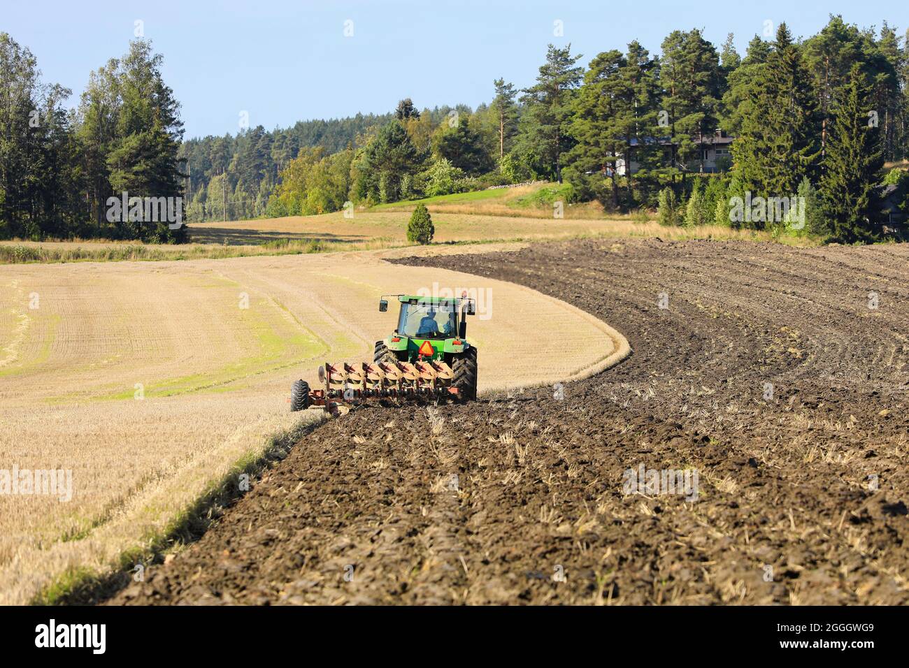 Tractor John Deere y arado trabajando en campo cosechado en un hermoso día soleado de principios de otoño. Salo, Finlandia. 29 de agosto de 2021. Foto de stock