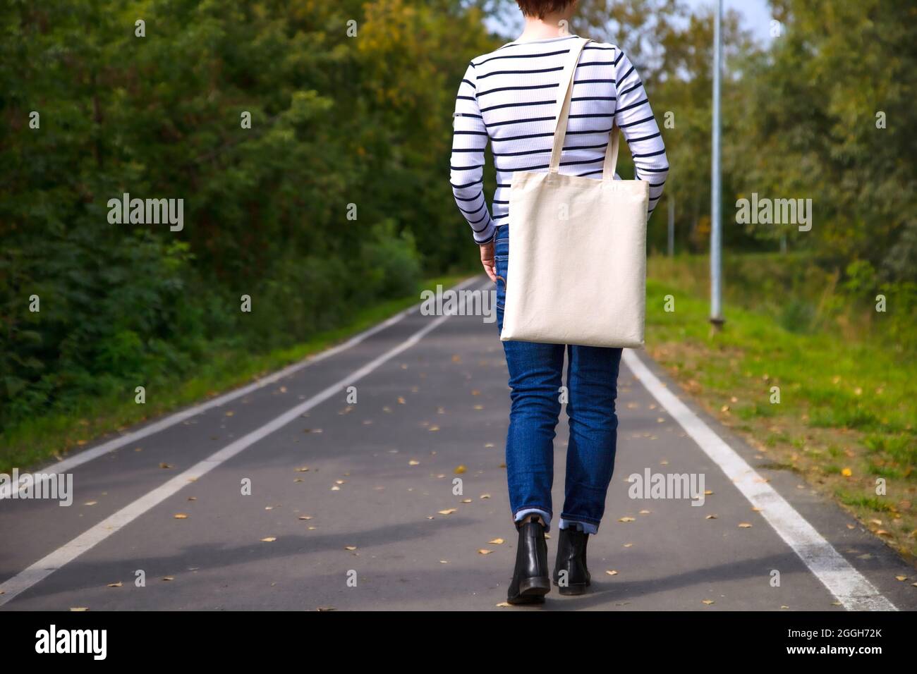 Mujer en camiseta blanca a rayas con bolsa de compra vacía y reutilizable. Bolsa de mano femenina de lona ecológica mofada Foto de stock