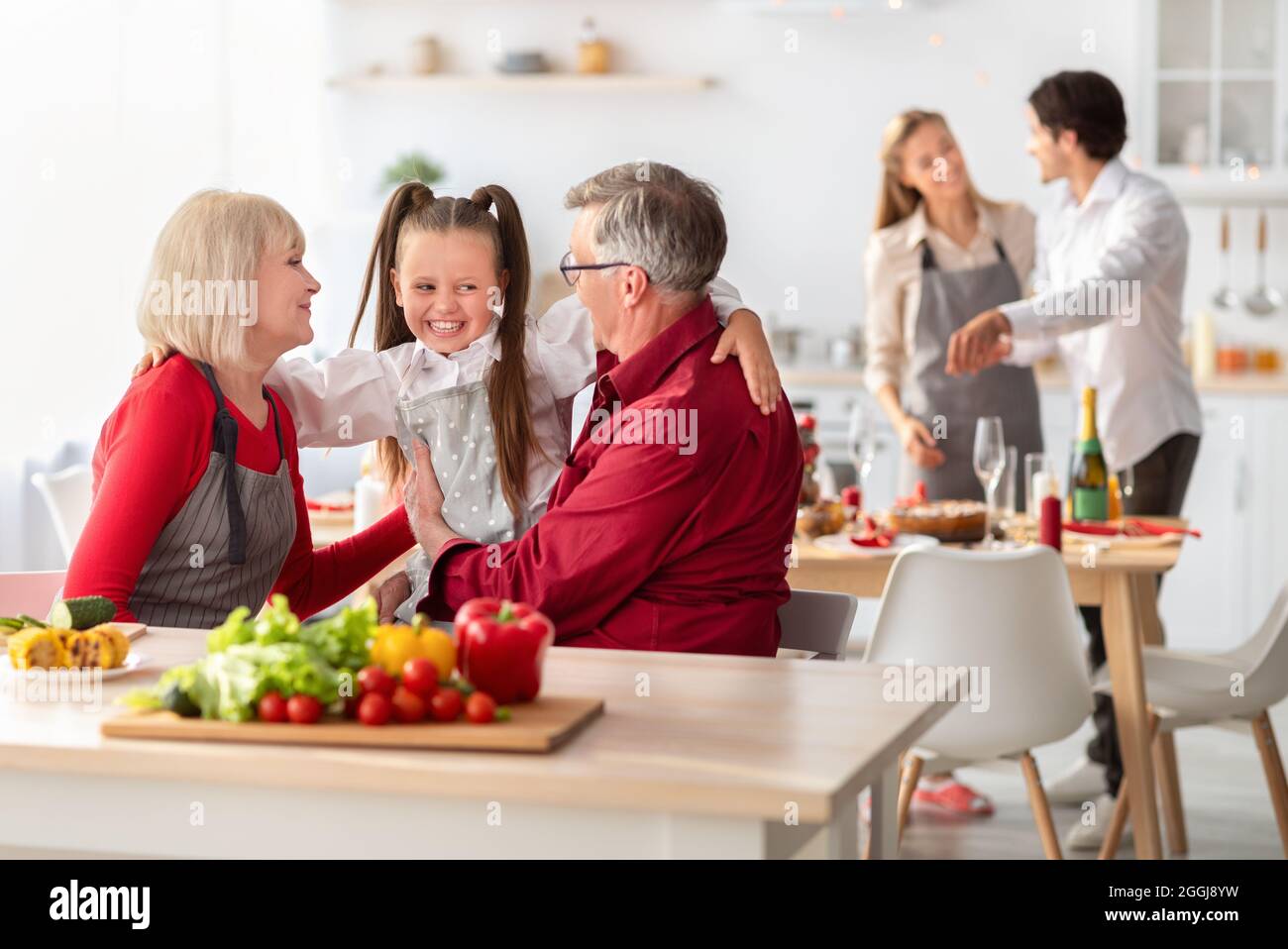 Enamorados abuelos abrazando a su linda nieta mientras cocinaba una cena festiva en casa Foto de stock