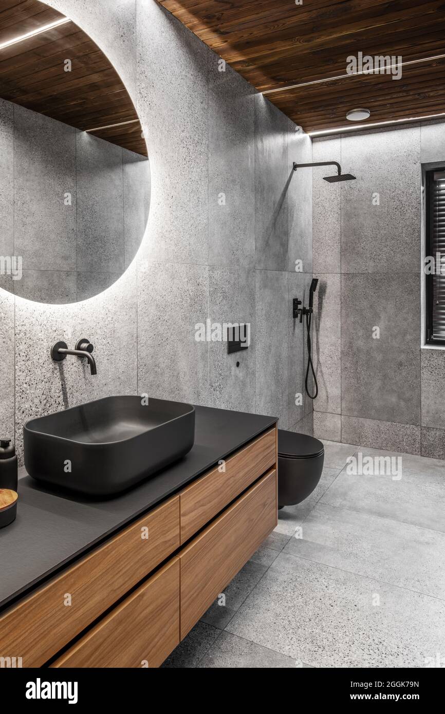 Moderno cuarto de baño minimalista con azulejos grises de piedra, muebles  de madera, lavabo y aseo negro y espejo redondo. Concepto de cuarto de baño  de spa Fotografía de stock - Alamy