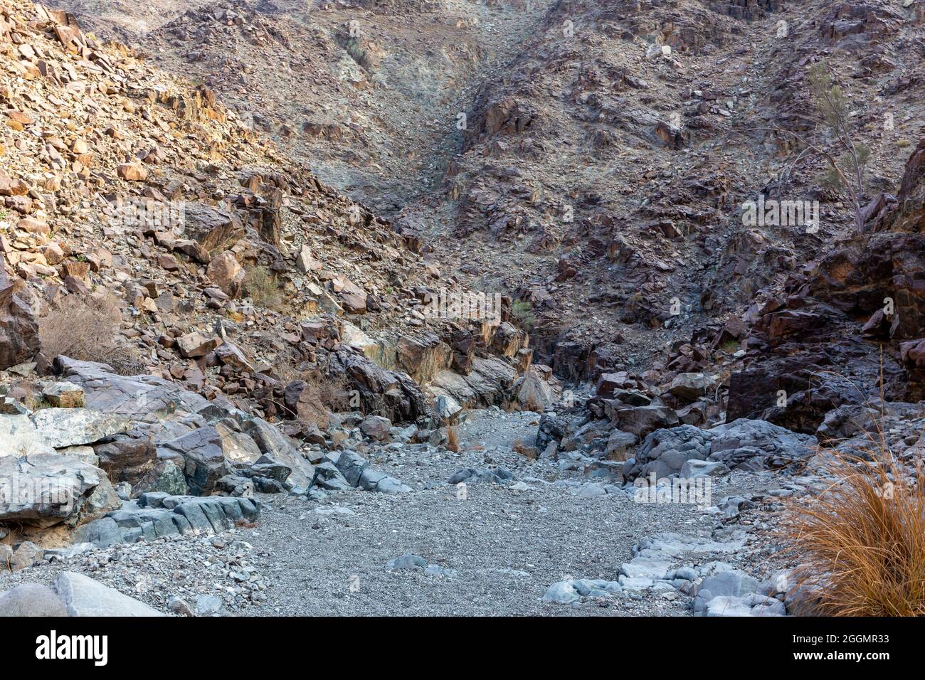 Stony, lecho seco del río (wadi) con restos de mineral crudo de cobre, piedras verdes y rocas, ruta de senderismo de cobre, Hatta, Hajar Mountains, EAU. Foto de stock