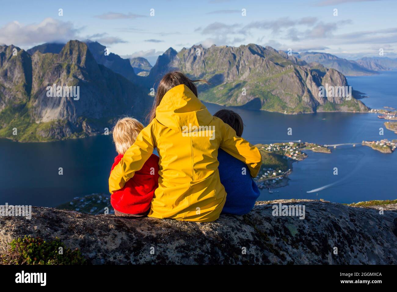 Mujer con chubasquero amarillo y su hijo, disfrutando de una vista  espléndida de los fiordos desde el sendero de Treeking de Reinebringen,  gente en la cima de la montaña mirando Fotografía de