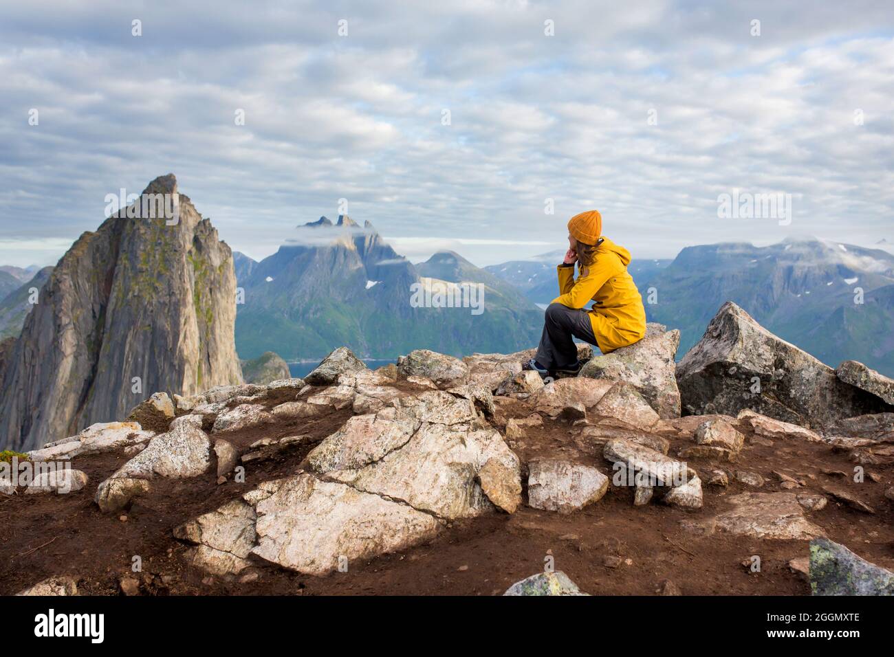 Mujer con chubasquero amarillo, sentada al revés sobre una roca y mirando  sobre la montaña Segla en la isla Senja, Noruega del Norte. Increíble  paisaje hermoso y s Fotografía de stock - Alamy