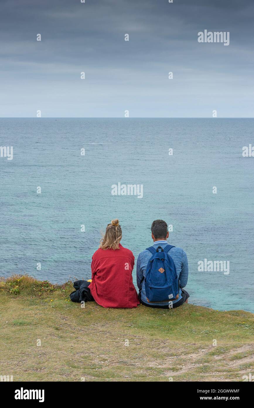 Una pareja de vacaciones sentados juntos en la costa de Newquay con vistas al Mar Celta. Foto de stock