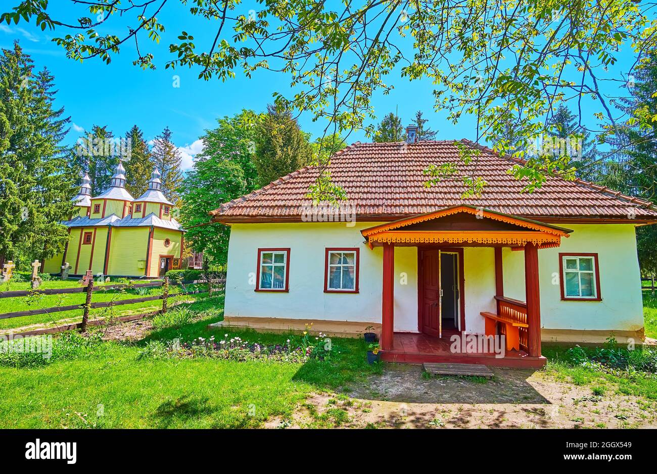 La casa del sacerdote de la aldea con la iglesia de madera en el fondo, Pereiaslav Scansen, Ucrania Foto de stock