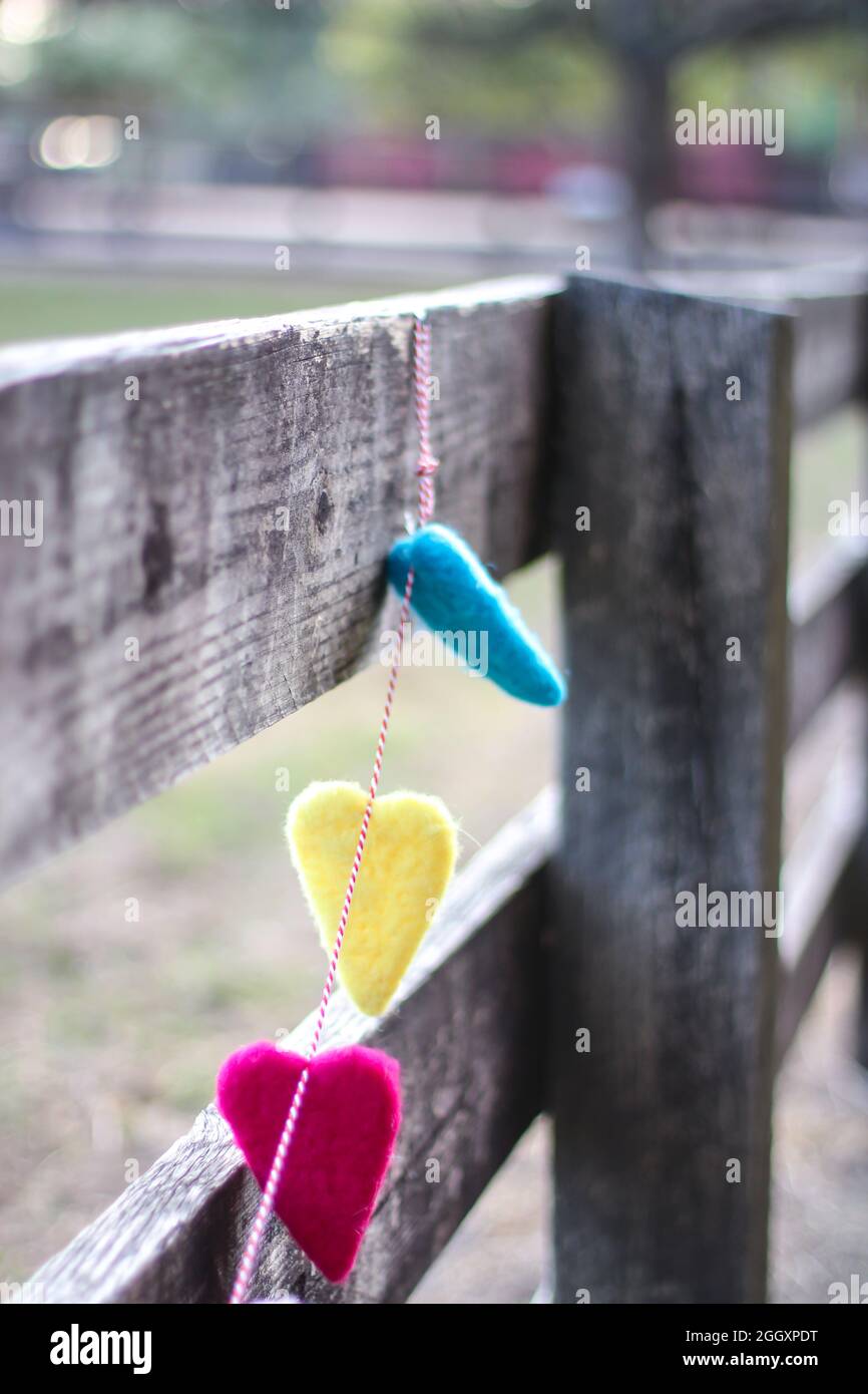 Una guirnalda de color arco iris hecha de corazones colgando de una valla de madera. Foto de stock