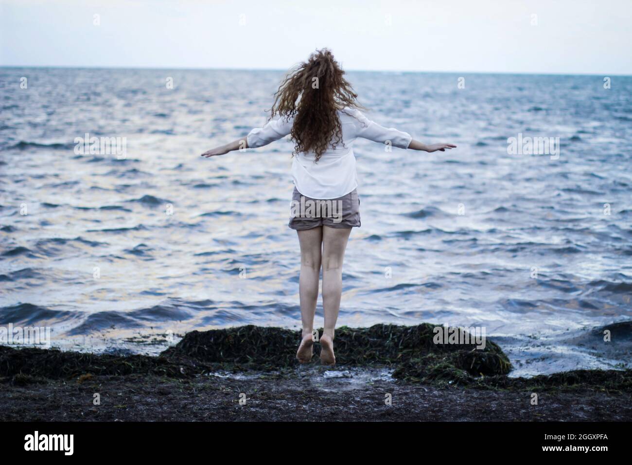 Mujer caucásica pelirroja saltando a la orilla de la playa, haciendo ejercicio, yoga, levitando Foto de stock