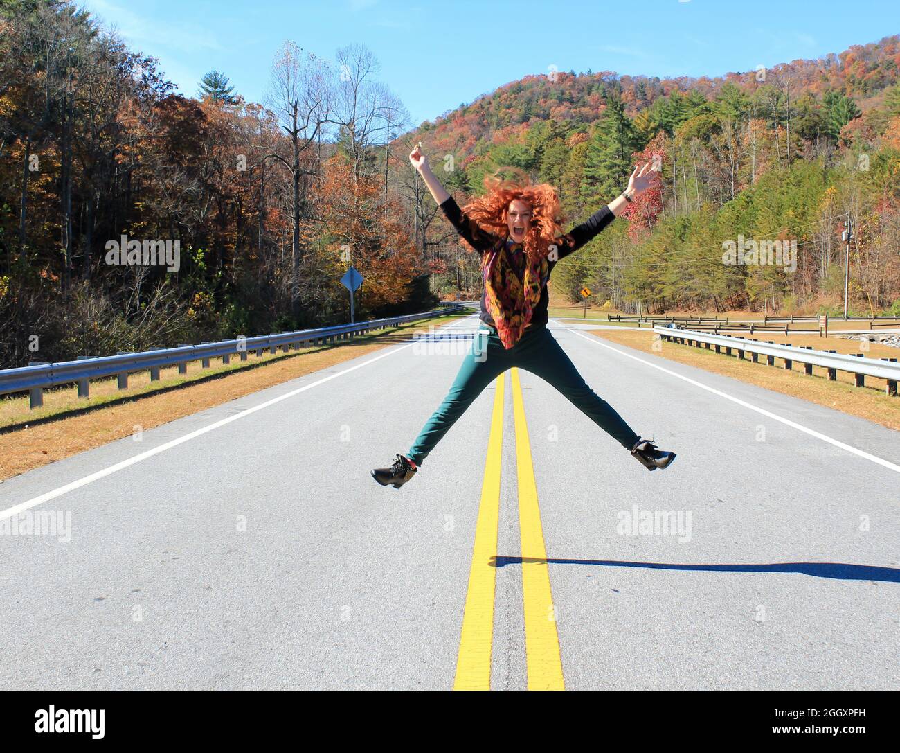 Mujer caucásica pelirroja saltando en medio de la calle en las montañas. Feliz y alegre Foto de stock