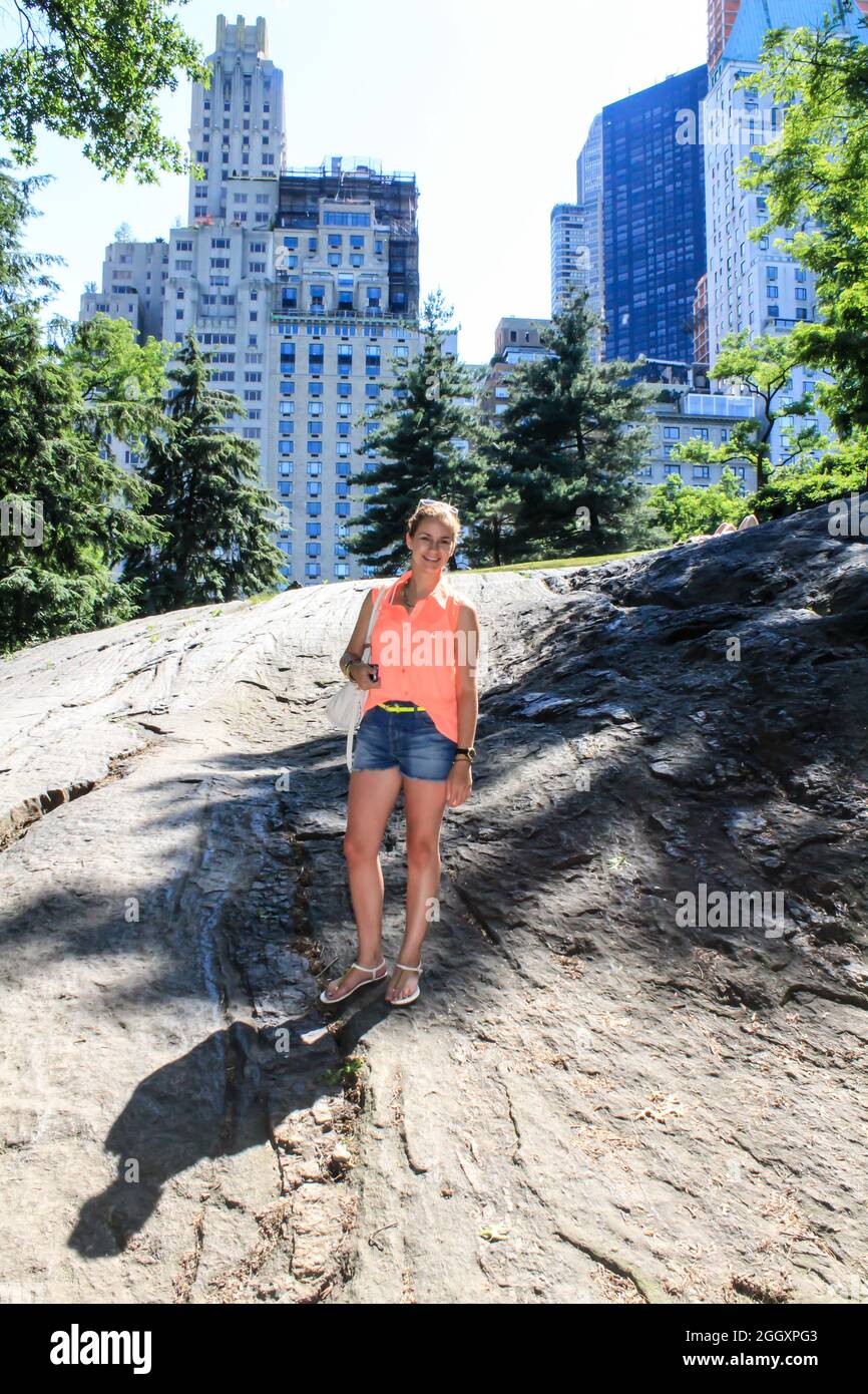Joven de pie en algunas rocas en Central Park frente a edificios en la ciudad de Nueva York. Foto de stock