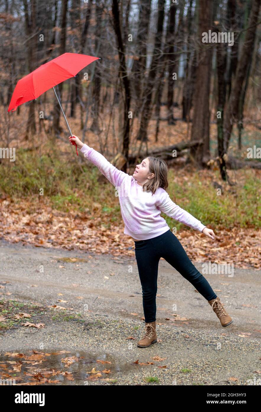 La joven lucha por aferrarse a un paraguas rojo en un día ventoso Foto de stock