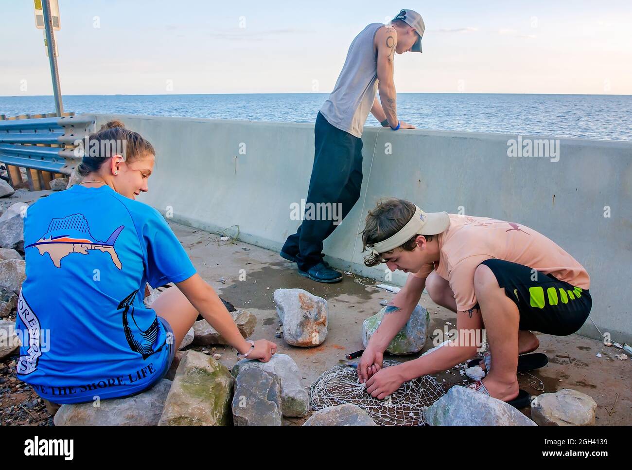 Un adolescente trabaja en una red de cangrejos de doble anillo mientras él y sus amigos pescan desde un puente dañado después del huracán Nate, 11 de octubre de 2017, en Coden, Alabama. Foto de stock