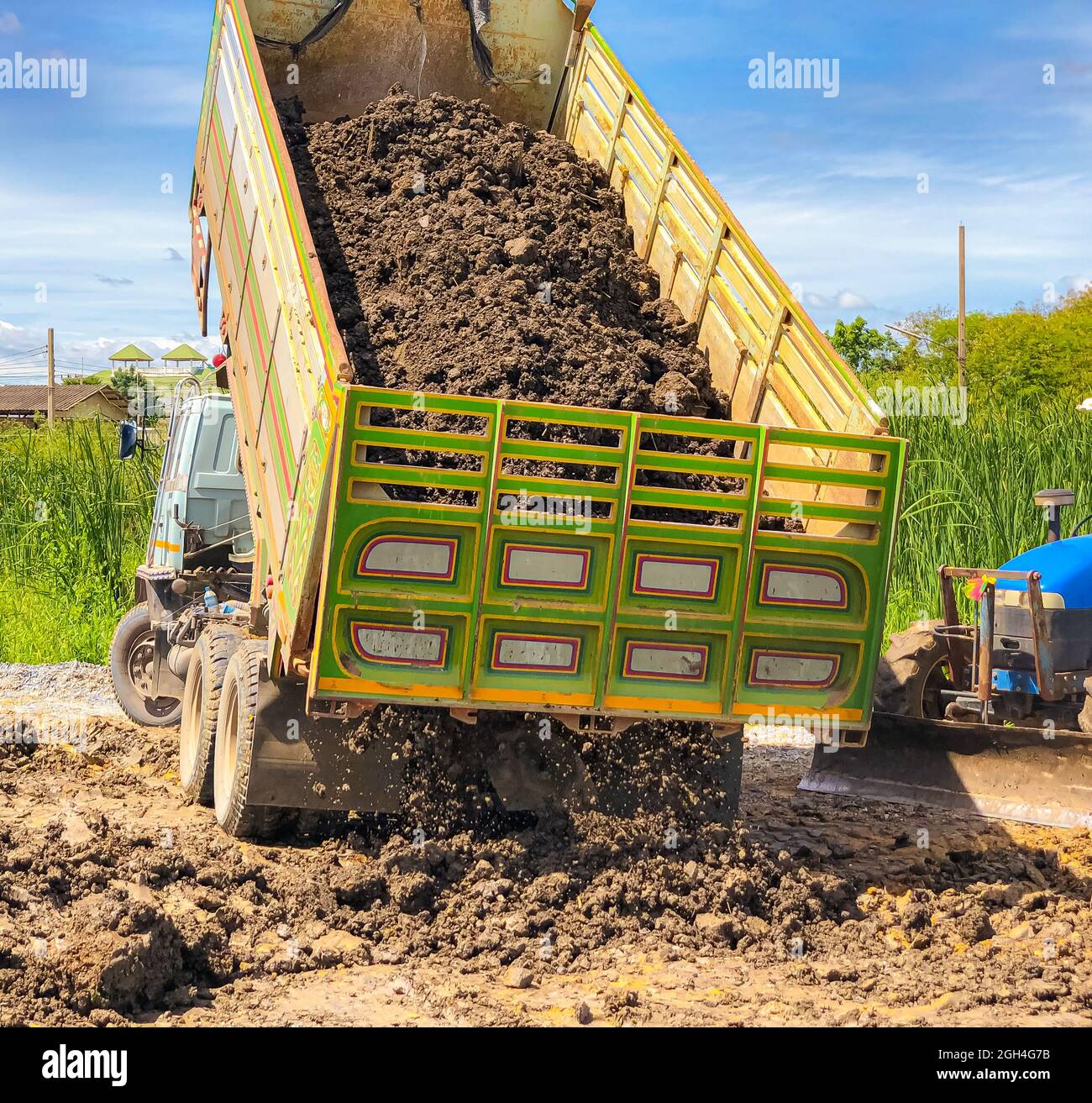 Un camión volquete lo suficientemente grande como para transportar esa cantidad de tierra, el muñero que vierte el soil.The thactor está listo para ajustar el suelo. Foto de stock