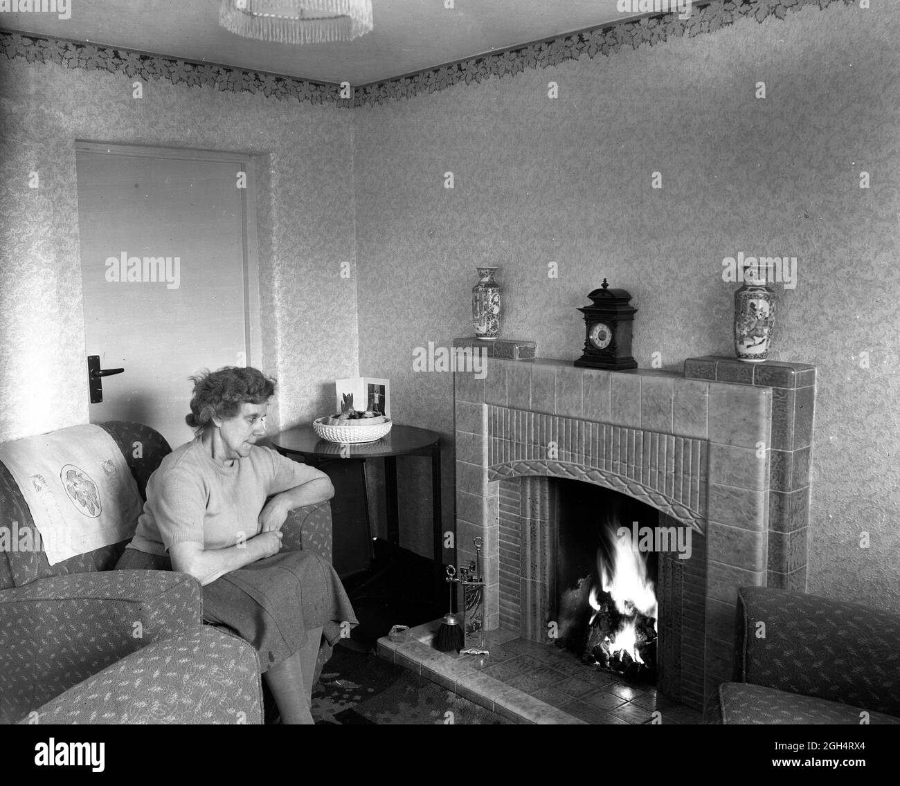 Hogar dulce hogar anciana sentada junto a su fuego de carbón en una casa del consejo Gran Bretaña 1952 Foto de stock