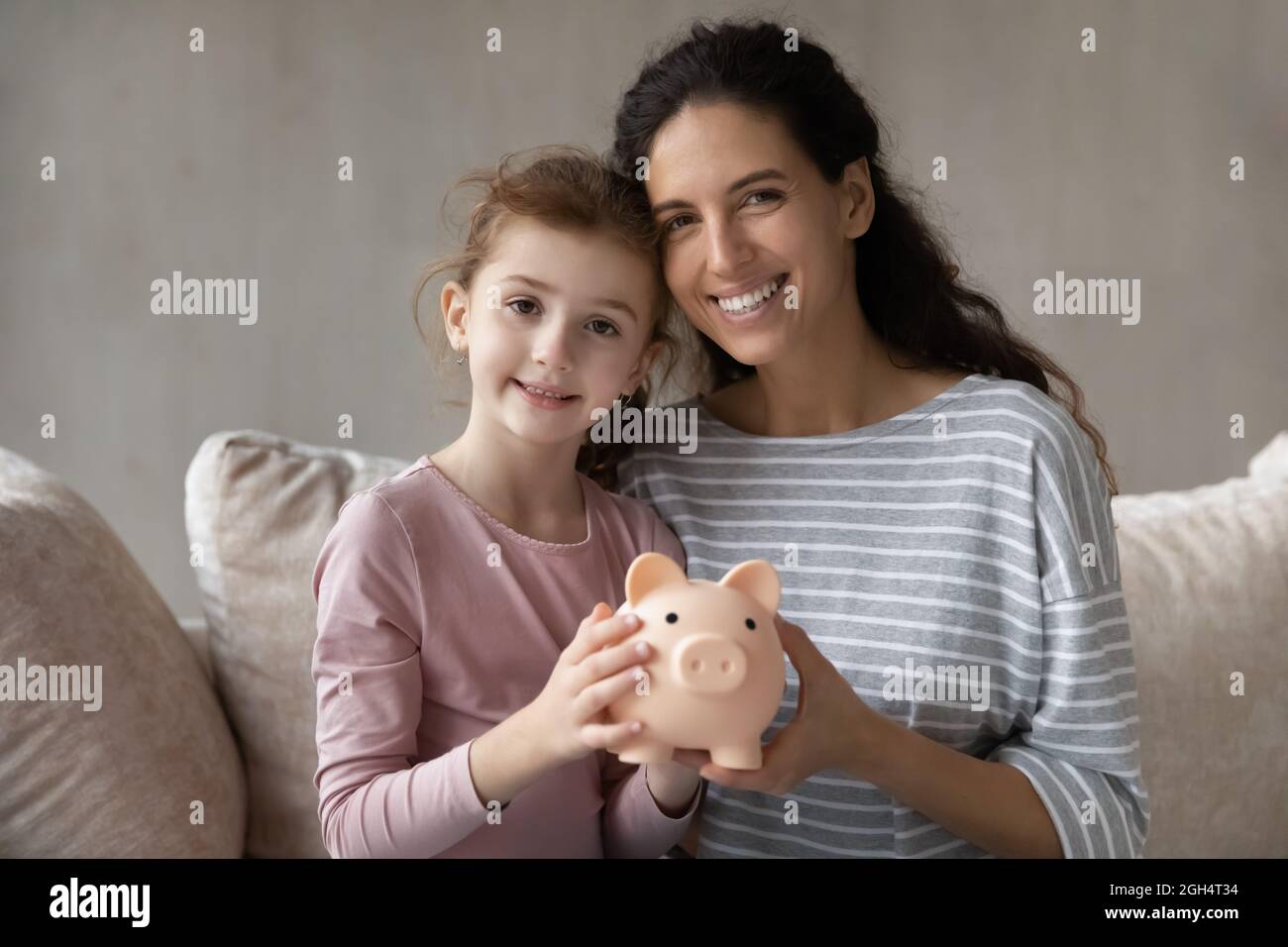 Madre joven sonriente y niño pequeño sosteniendo un banco de cerdos. Foto de stock